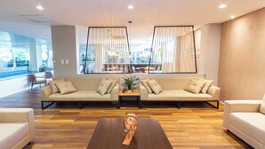 A modern lounge area with a large sofa set, a wooden coffee table, and a view of the city through large windows.