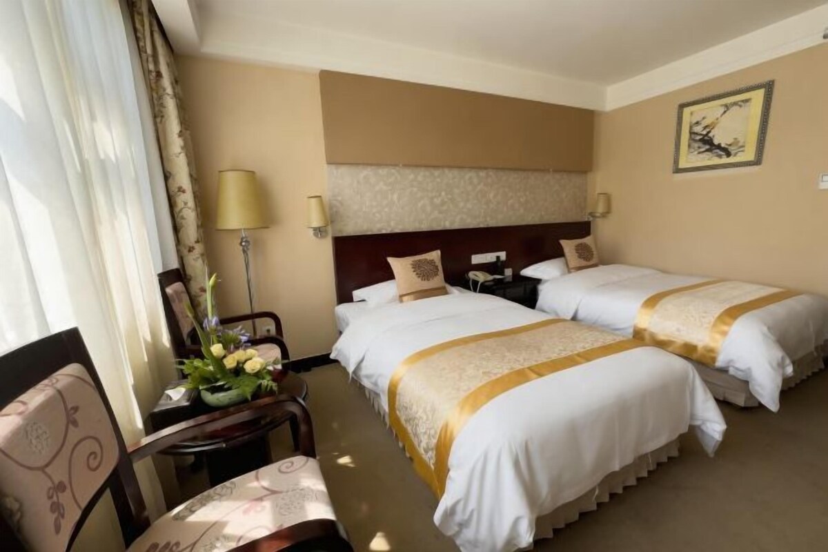 A hotel room with two beds, a desk, a chair, and a lamp.