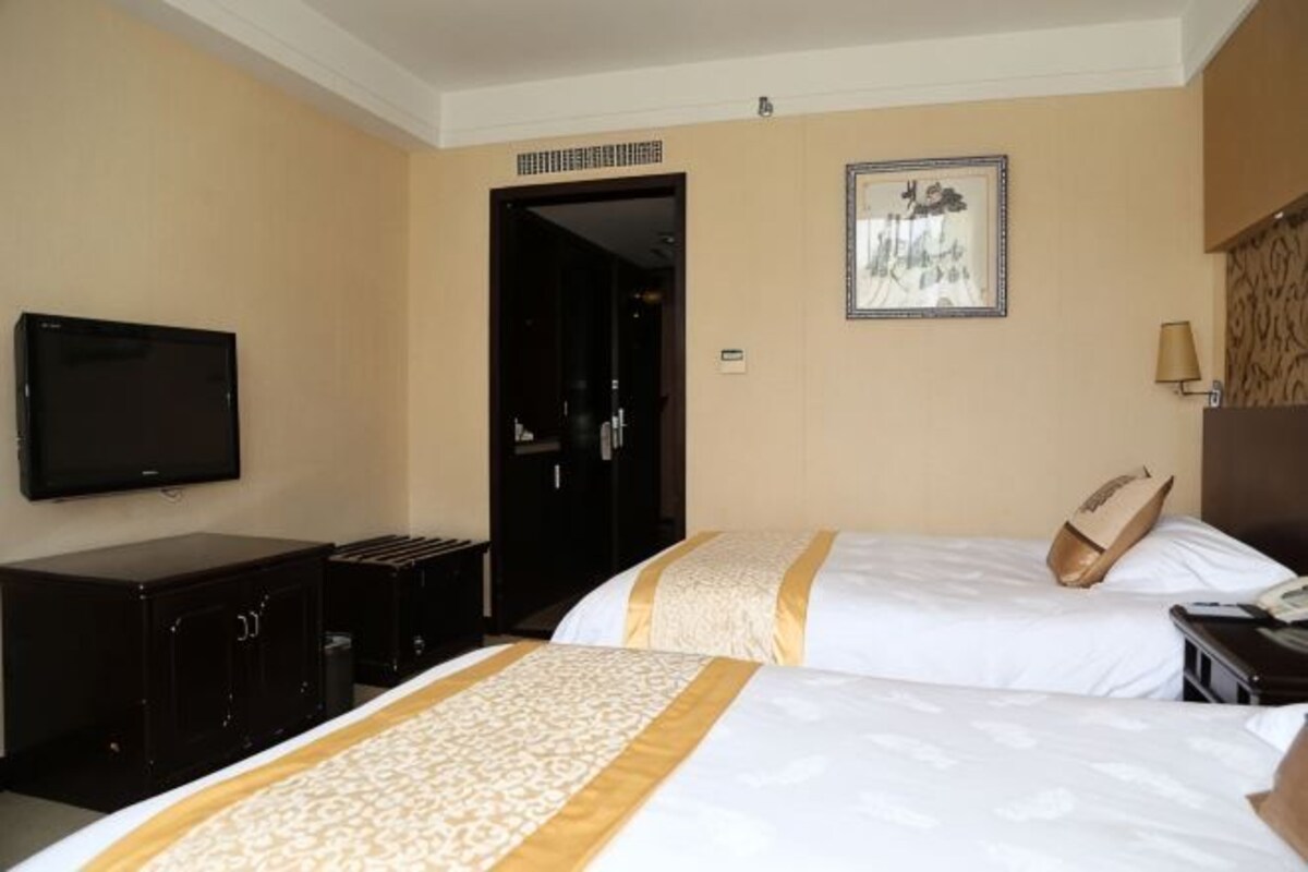 A hotel room with two beds, a TV, a desk, and a door leading to a hallway.