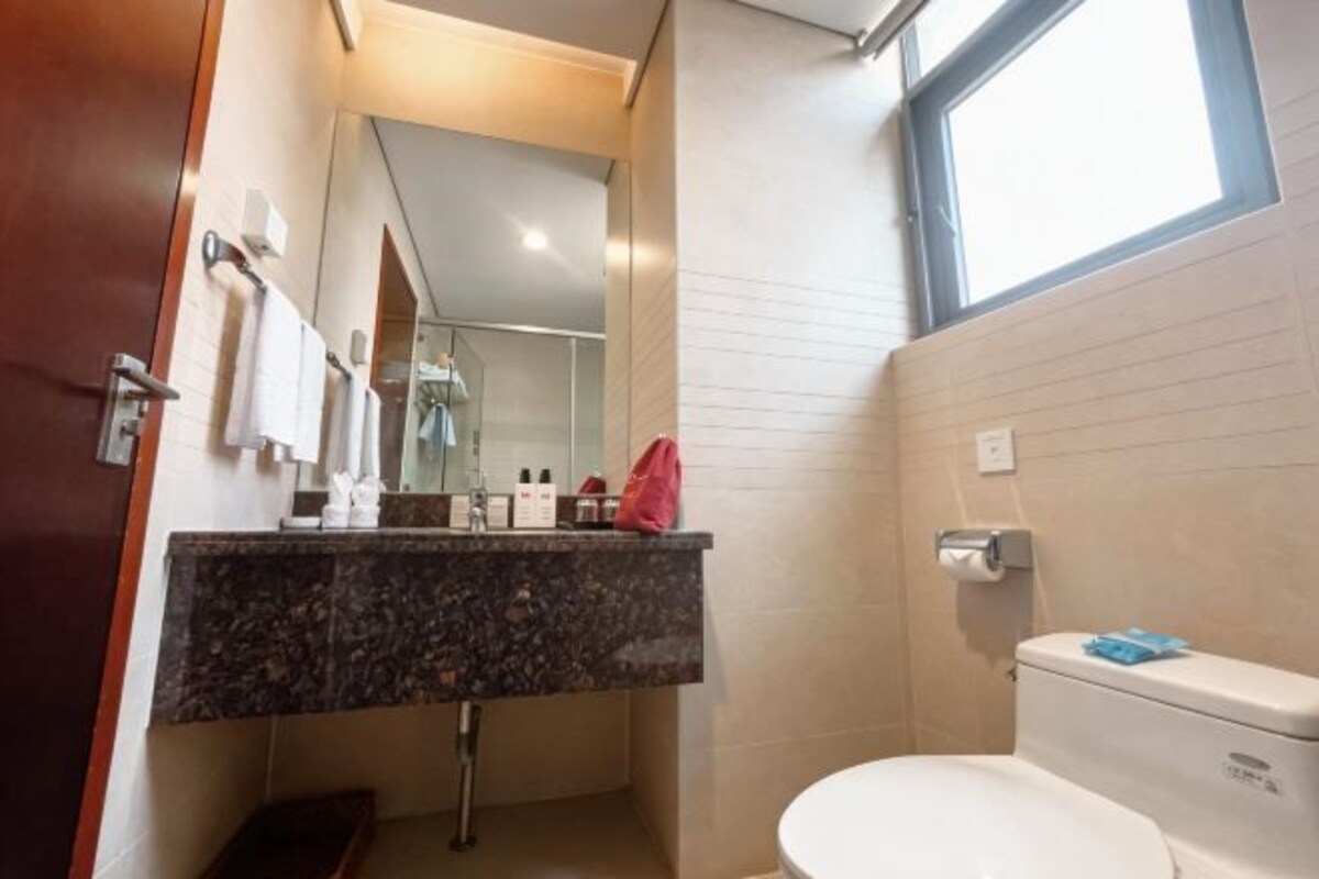 A bathroom with a marble sink, a toilet, a mirror, and a window.