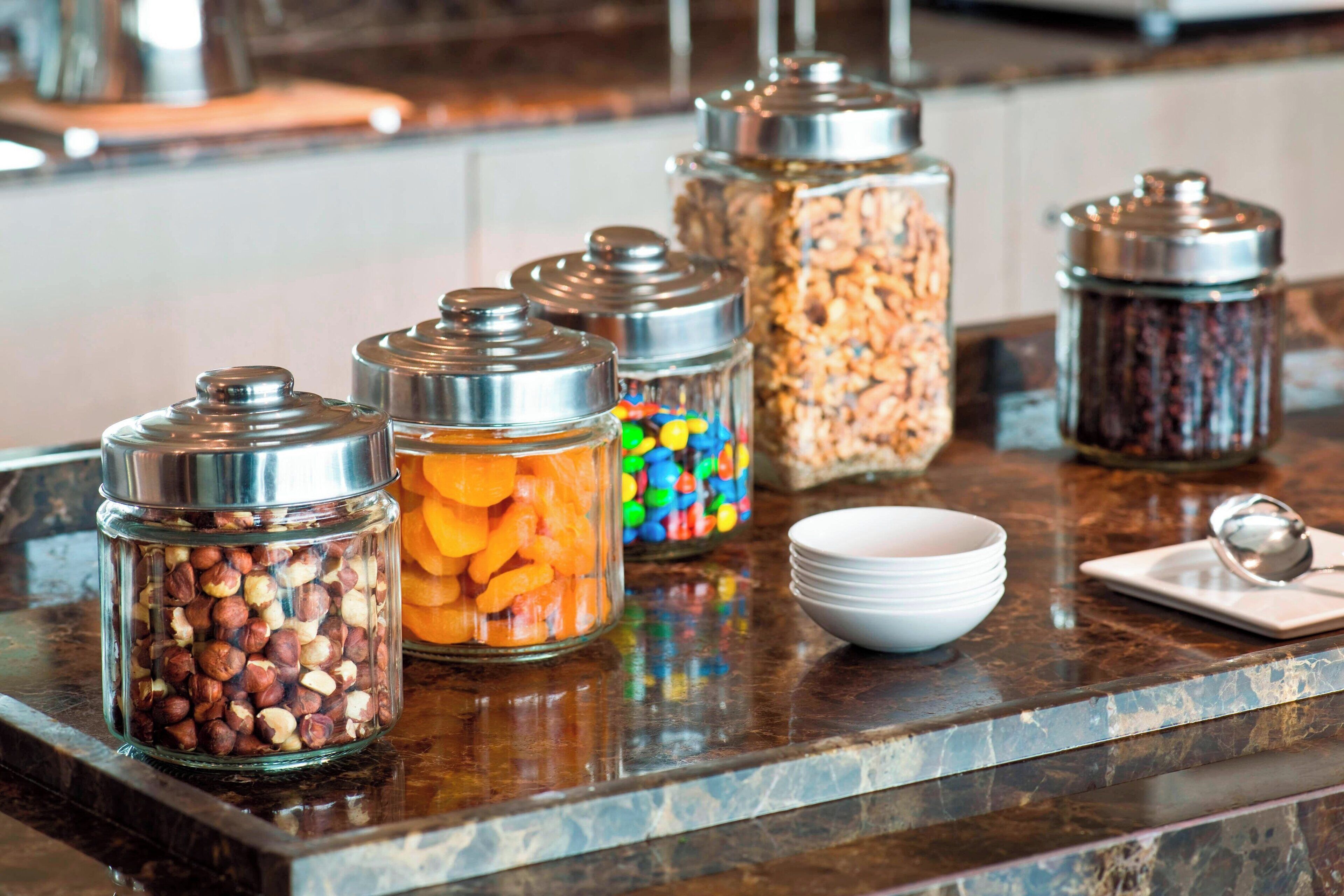 A buffet setup with various food items in glass containers on a marble countertop.