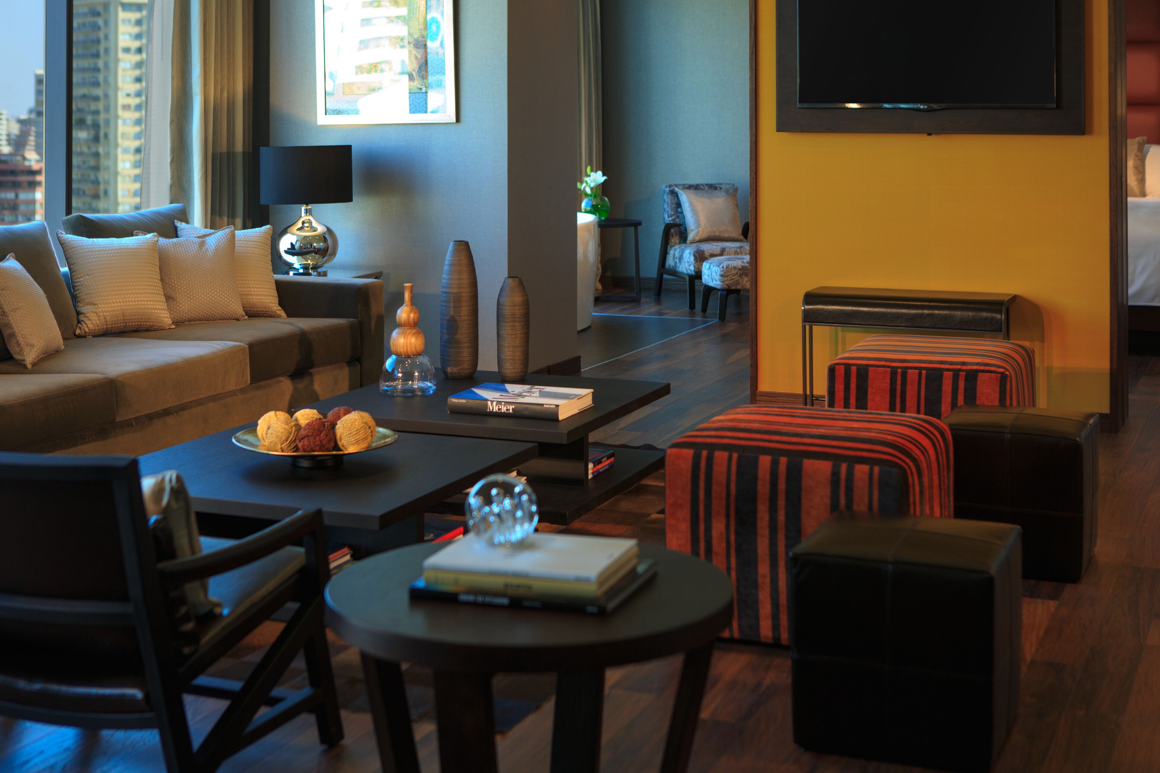 A modern living room with a sofa, coffee table, ottomans, and a TV.