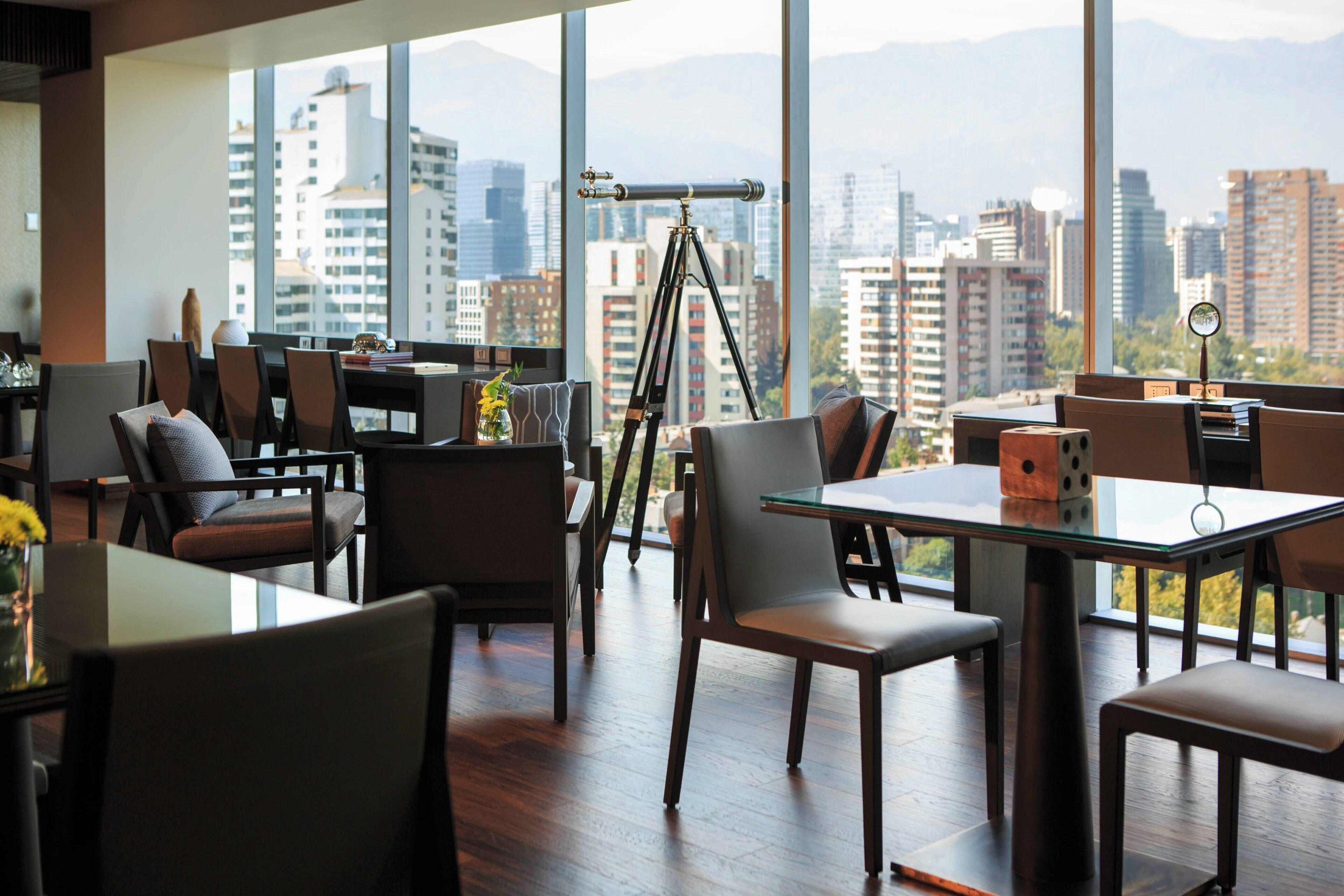 A modern dining area with a city view, large windows, and a telescope.
