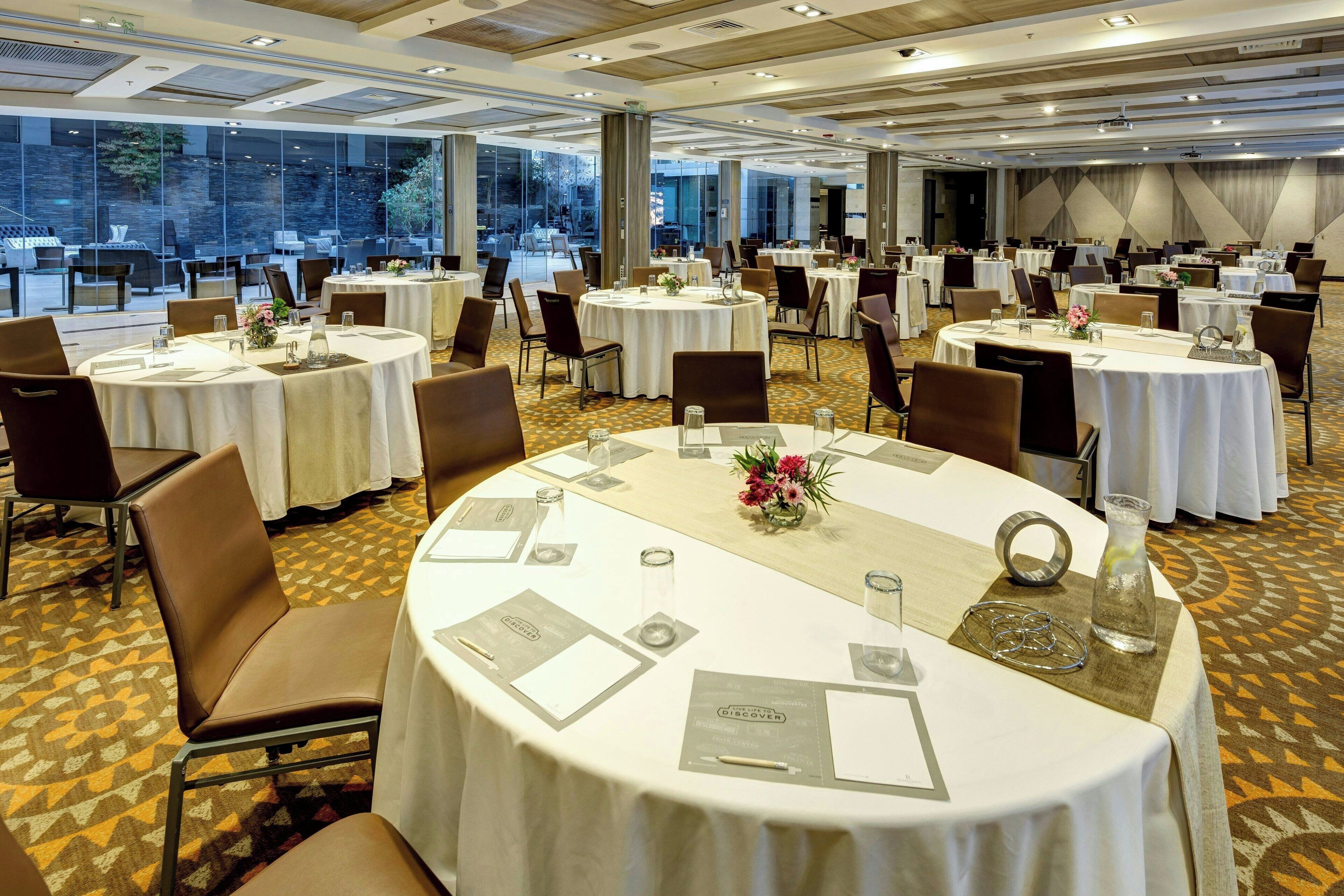 Un salón de banquetes con mesas redondas, sillas y piso alfombrado.