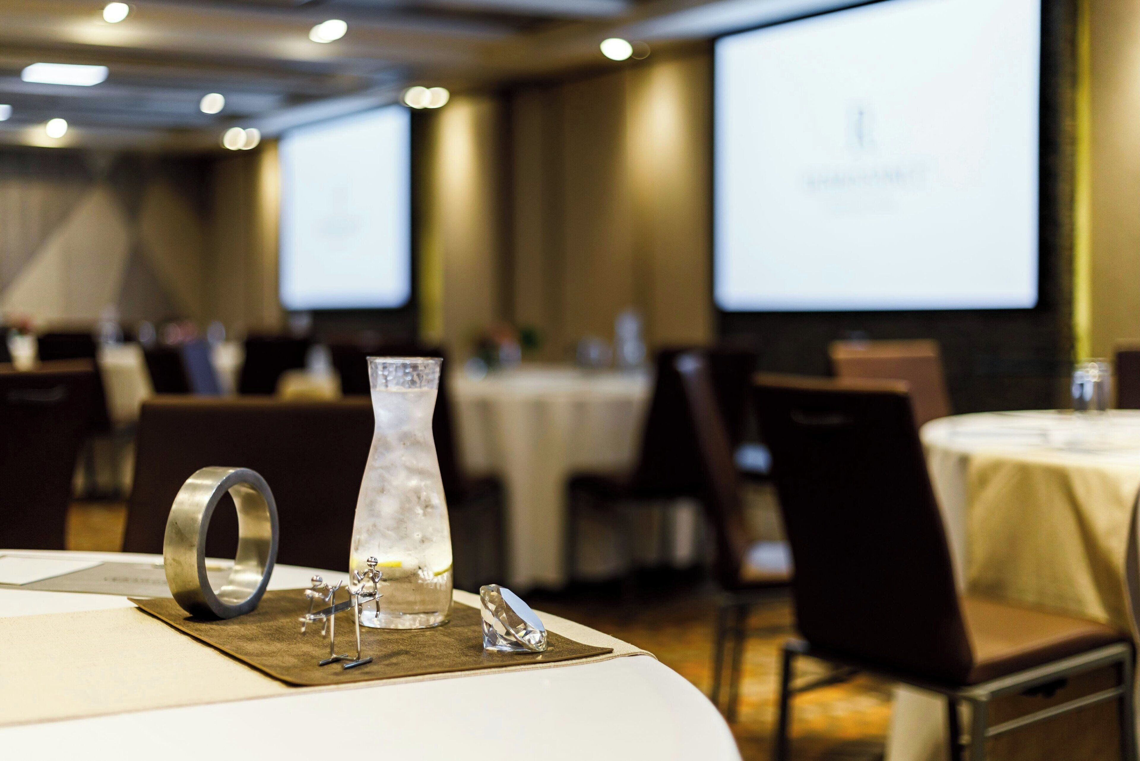Une salle de conférence avec des tables disposées pour une réunion, un écran de projection et un vase décoratif posé sur la table.