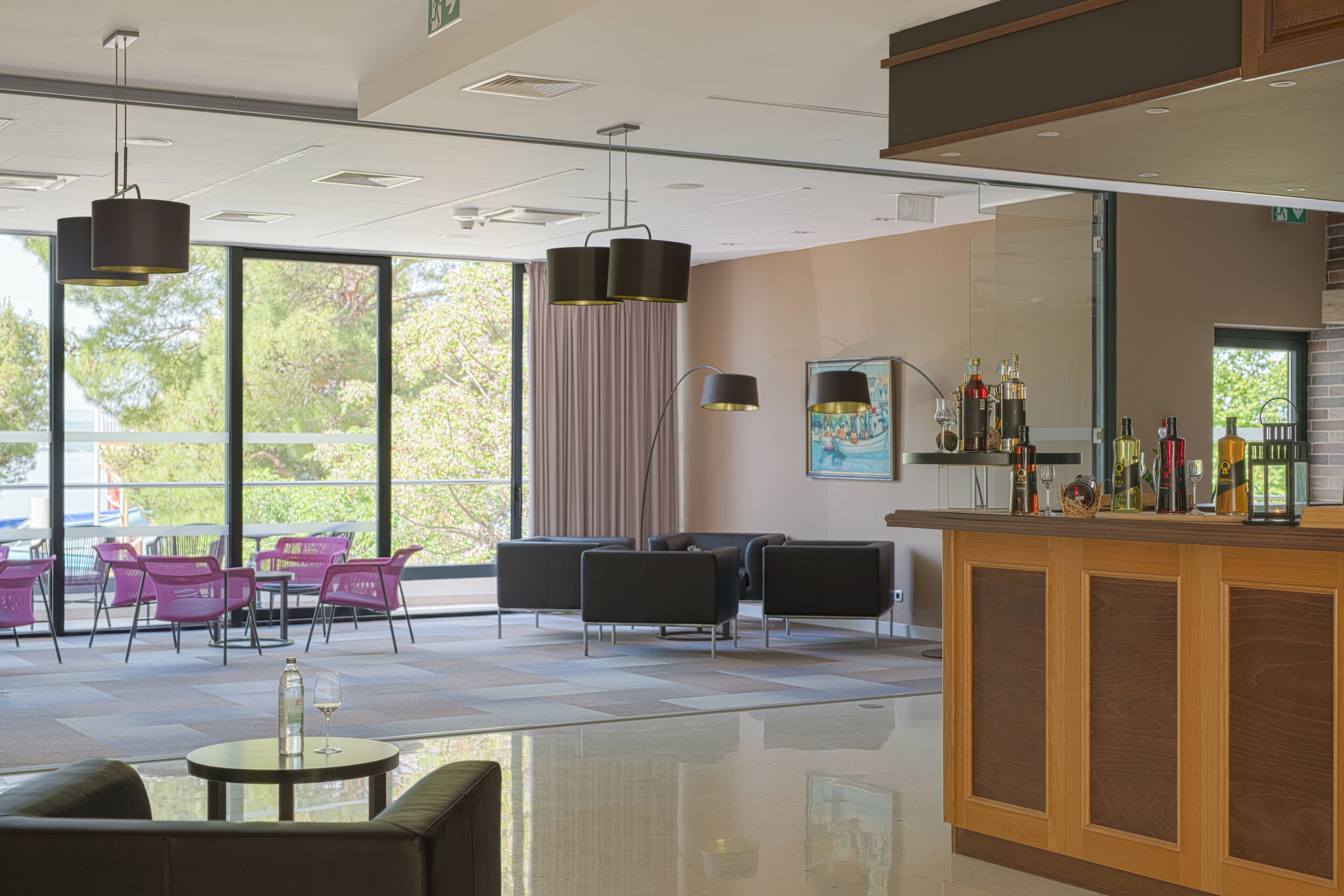 A modern hotel lobby with a bar area, seating with a view, and a large window.
