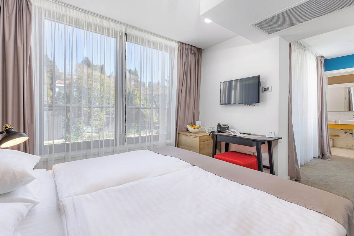 Een hotelkamer met een bed, een bureau, een televisie en een raam met gordijnen.