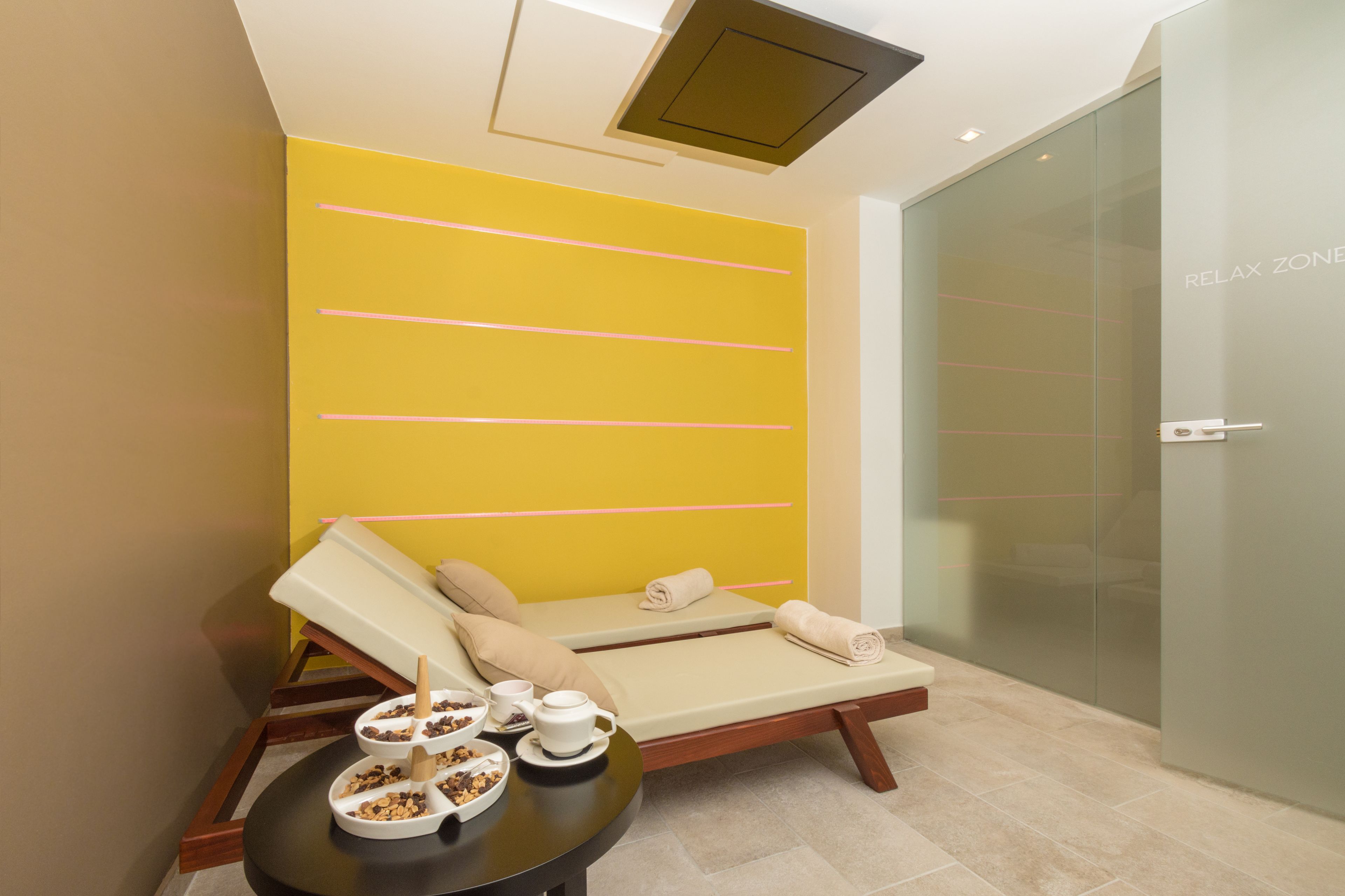 A spa room with a yellow wall, a massage table, and a small table with snacks and a teapot.