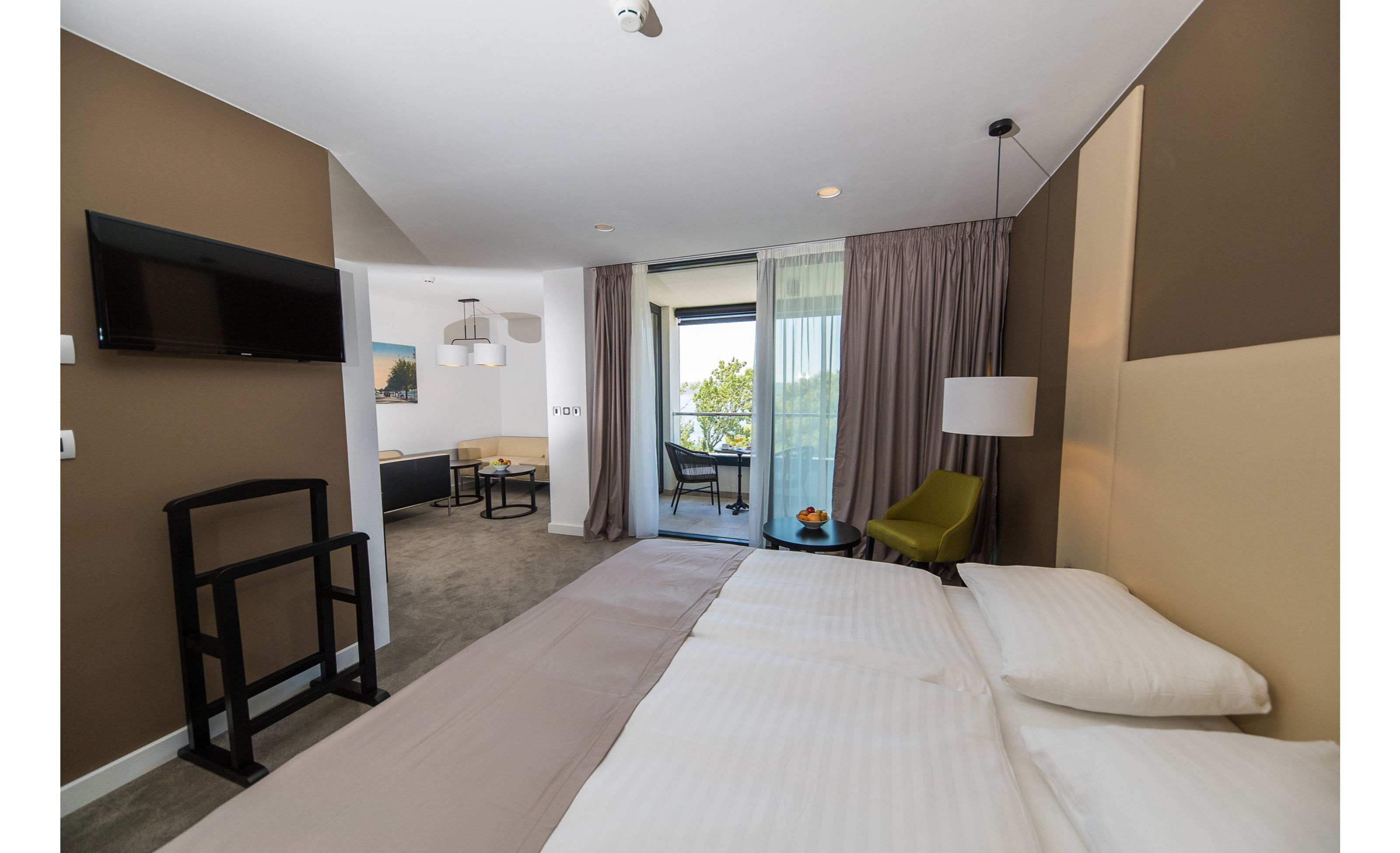 A hotel room with a bed, a desk, a chair, a TV, and a balcony with a view.