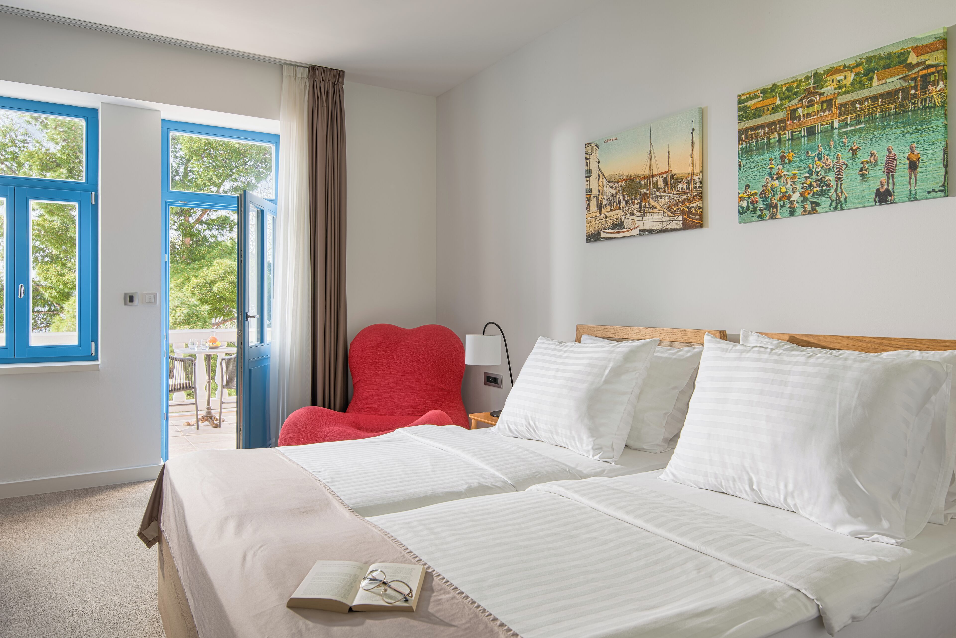 Ein Hotelzimmer mit zwei Betten, einem roten Sessel, einem Tisch und einem Bild an der Wand.