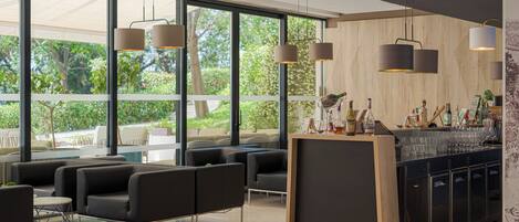 A modern bar area with a counter, seating, and large windows offering a view of greenery.