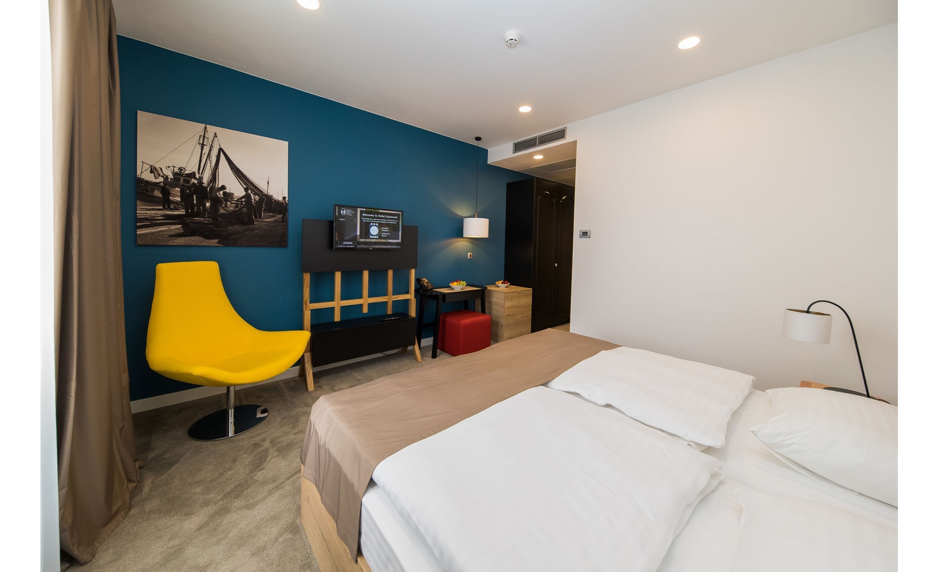 Een hotelkamer met een bed, bureau, stoel, televisie en een foto aan de muur.