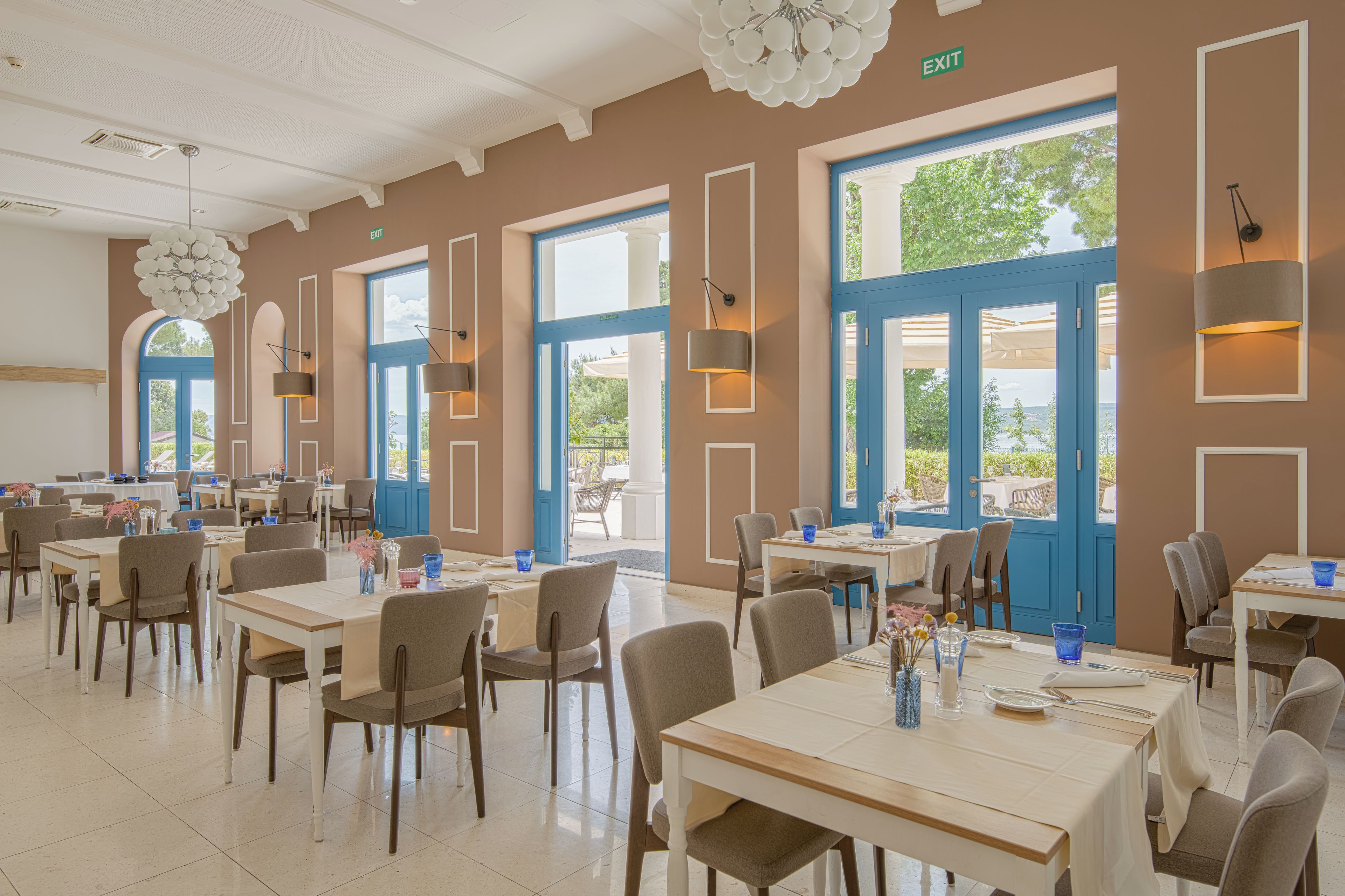 Un amplio comedor con varias mesas y sillas, ventanas grandes con marcos azules e iluminación moderna.