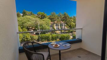 A balcony with a wicker chair and a small table, overlooking a residential area with trees and buildings.