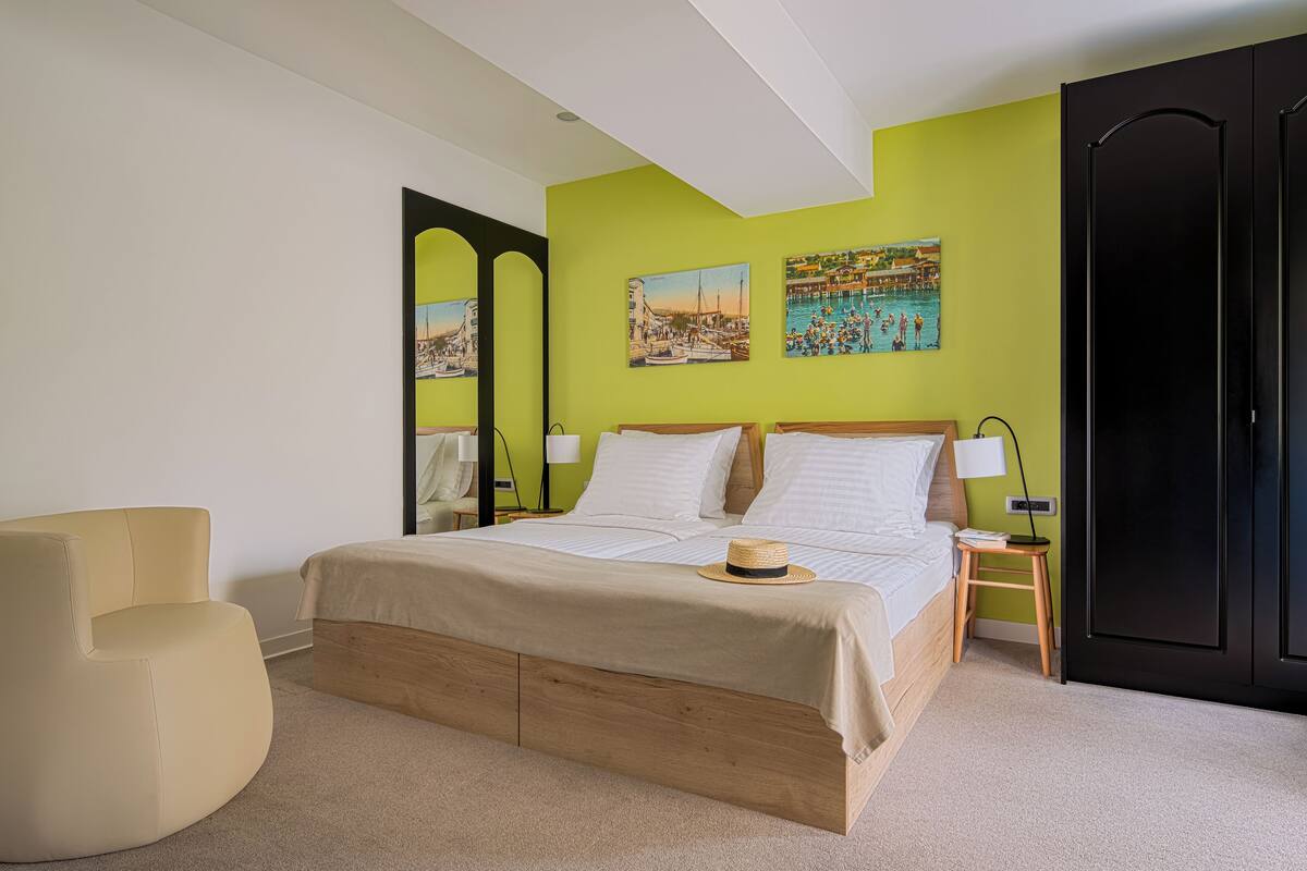 Une chambre à coucher avec un lit, une chaise, une table de chevet et deux tableaux accrochés au mur.