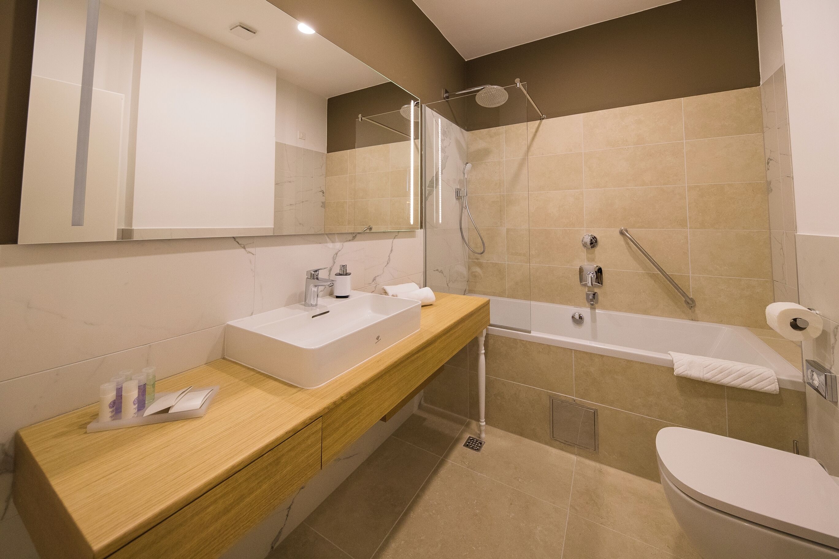 Une salle de bain moderne avec un meuble-lavabo en bois, un lavabo blanc, une cabine de douche en verre et une baignoire blanche.