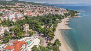 Vue aérienne d’une ville côtière avec une plage, des immeubles résidentiels et un hôtel doté d’une piscine et d’un espace de détente en plein air.