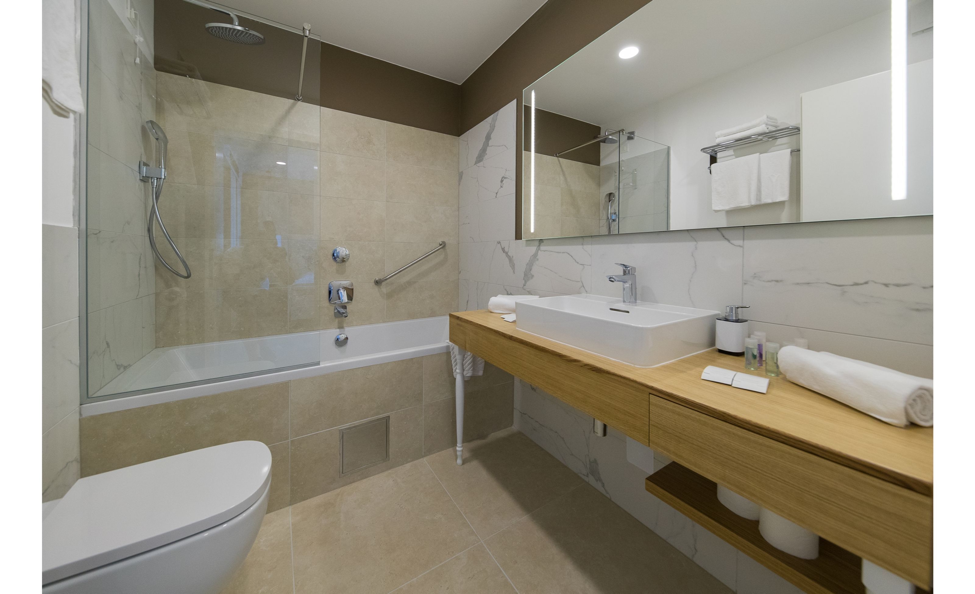A modern bathroom with a glass-enclosed shower, a white toilet, a wooden vanity with a sink, and a large mirror.