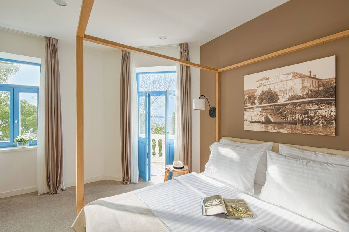 Une chambre d’hôtel avec un grand lit, une vue sur l’extérieur grâce à une porte vitrée et un tableau encadré au mur.