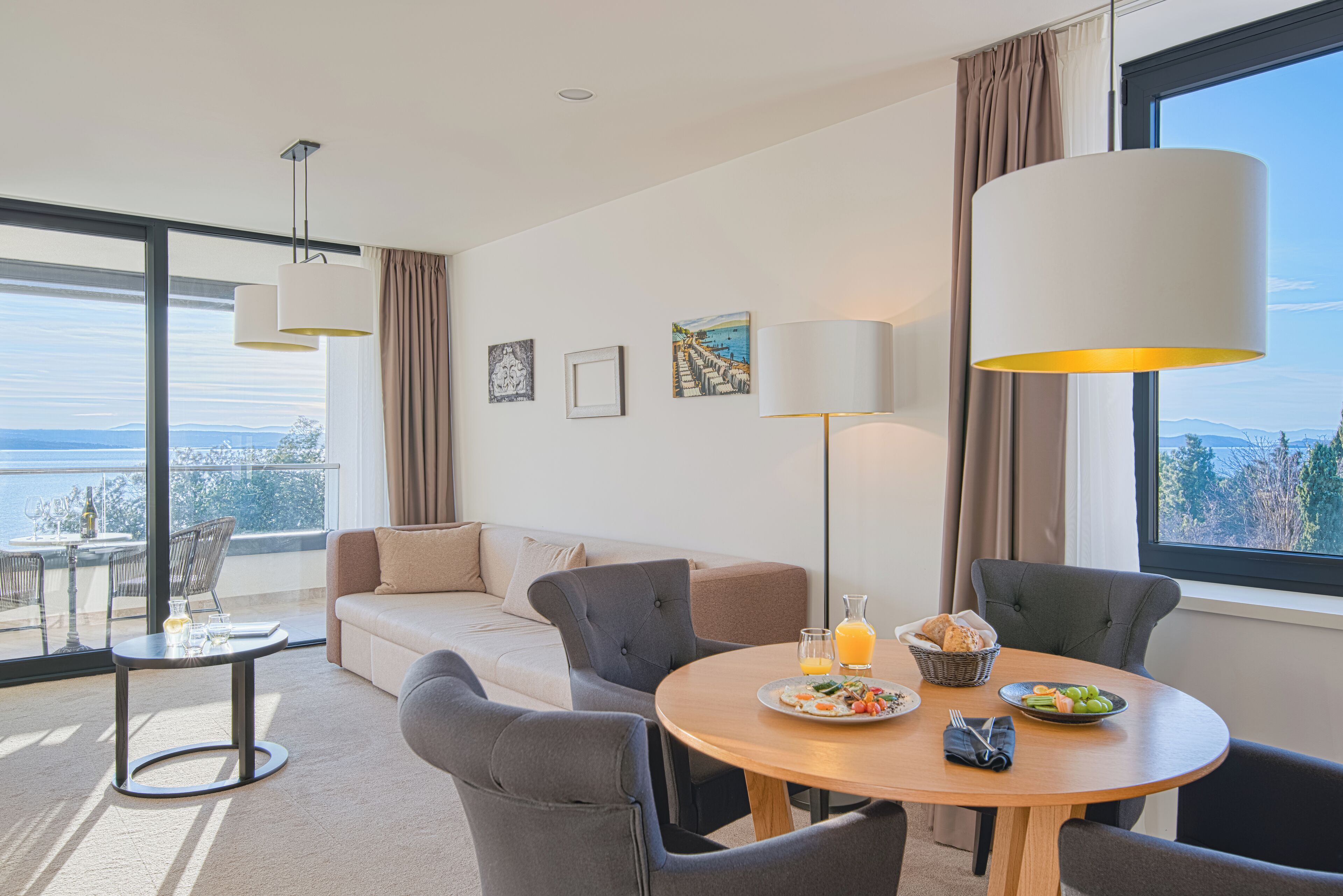 A modern hotel room with a balcony, a round dining table, and a sofa.