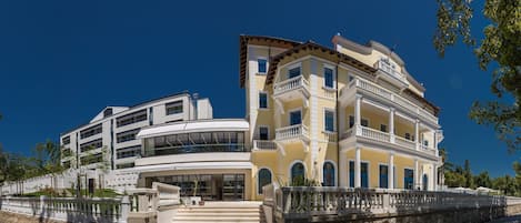 A multi-story hotel with a curved facade, balconies, and a stone staircase leading to the entrance.