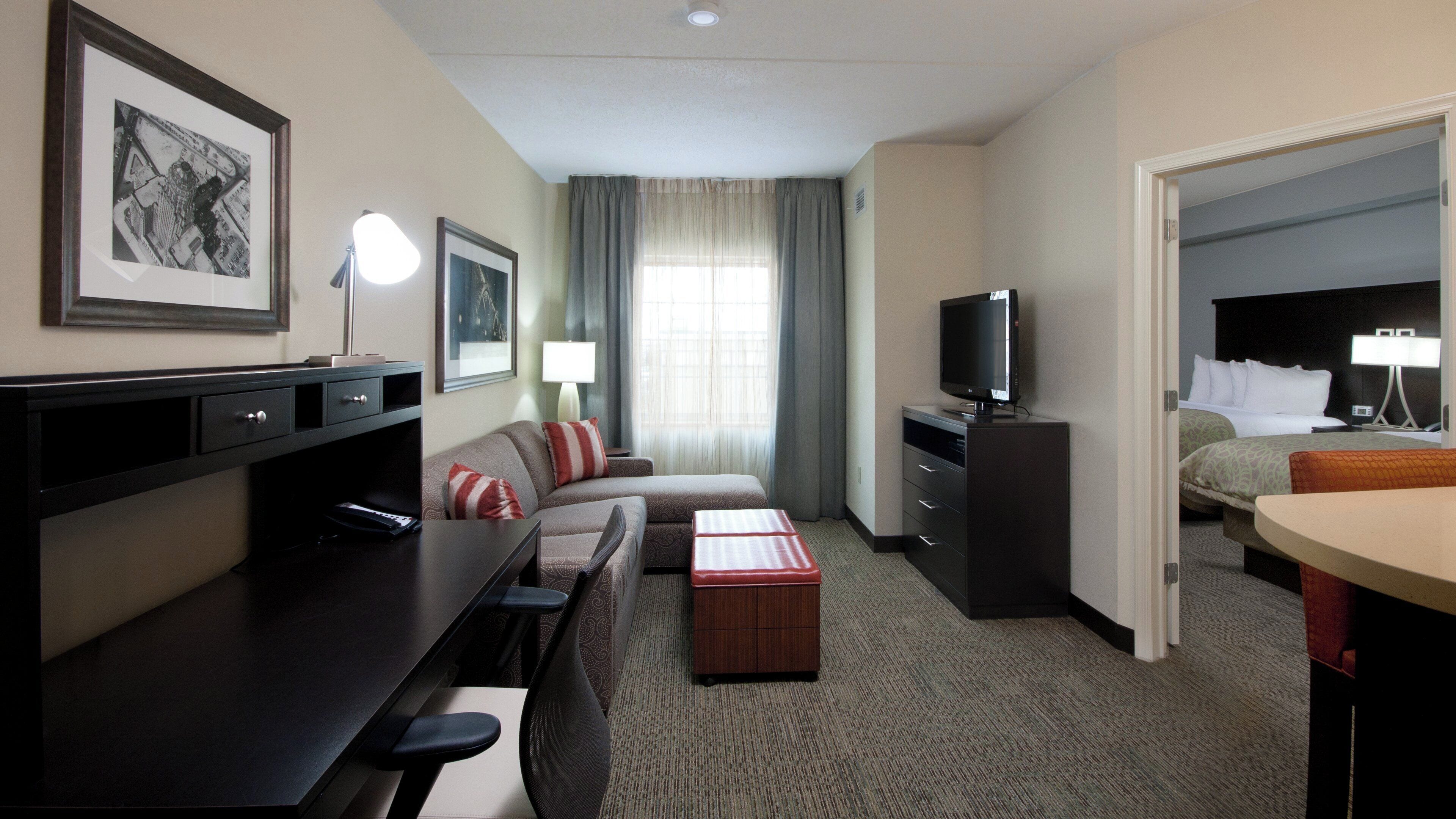Une chambre d’hôtel avec un canapé, une télévision, un bureau avec une lampe, une petite table et un lit.