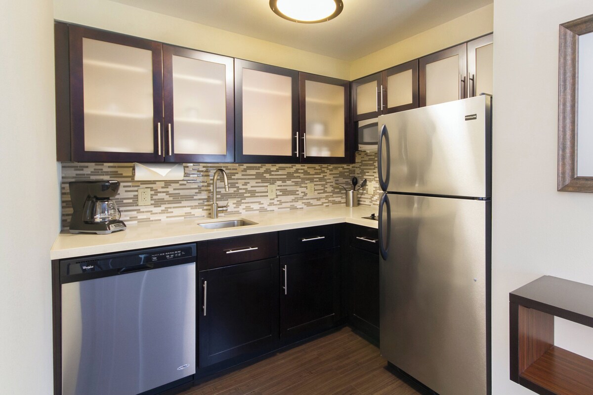 A compact kitchen with dark cabinets, a stainless steel refrigerator, a dishwasher, and a tiled backsplash.