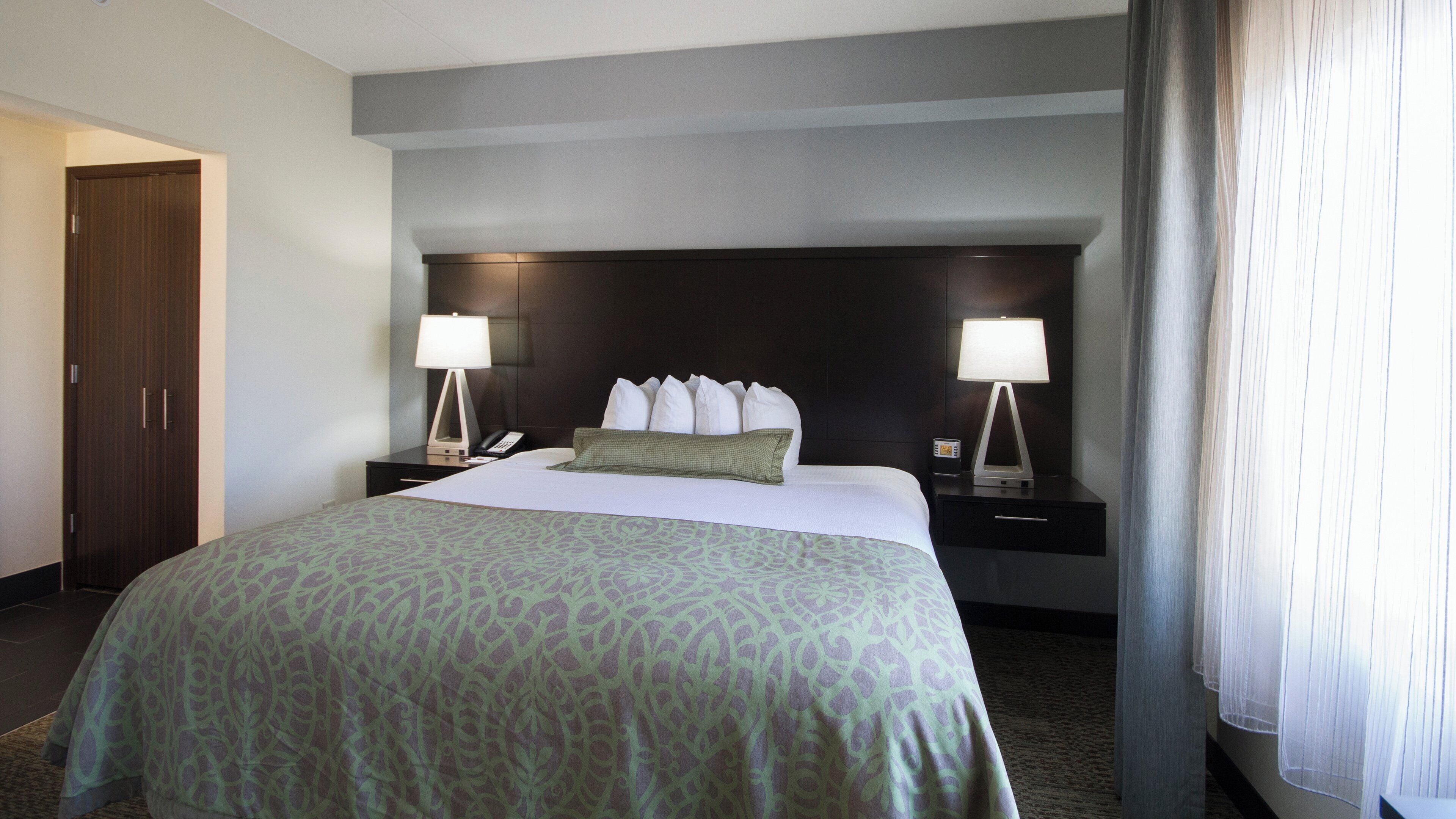 A hotel room with a large bed, two bedside tables with lamps, a telephone, and a dark headboard.