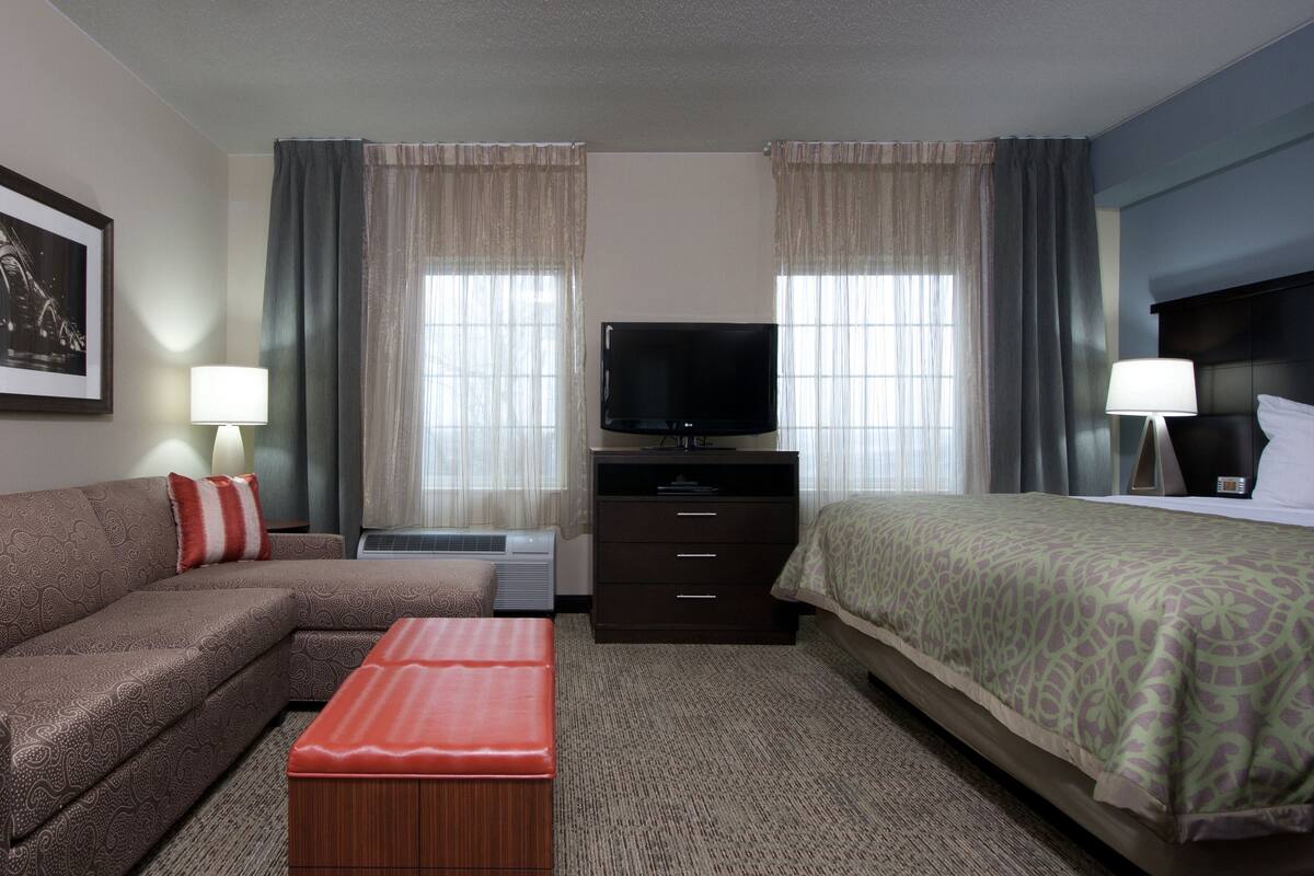 A hotel room with a sofa, a bed, a TV, a lamp, and a picture on the wall.
