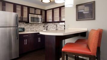 Una cocina moderna con armarios de madera oscura, electrodomésticos de acero inoxidable, encimera de mármol y una silla tapizada en rojo.