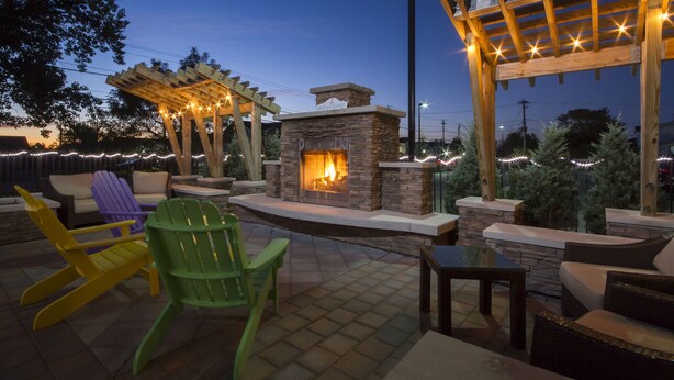 A patio area with a stone fireplace, outdoor seating, and string lights. - Staybridge Suites Buffalo-Amherst by IHG (Buffalo)