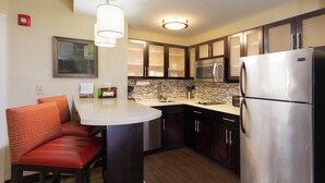 A compact kitchen with a refrigerator, microwave, and a small dining area with a chair. - Staybridge Suites Buffalo-Amherst by IHG (Buffalo)