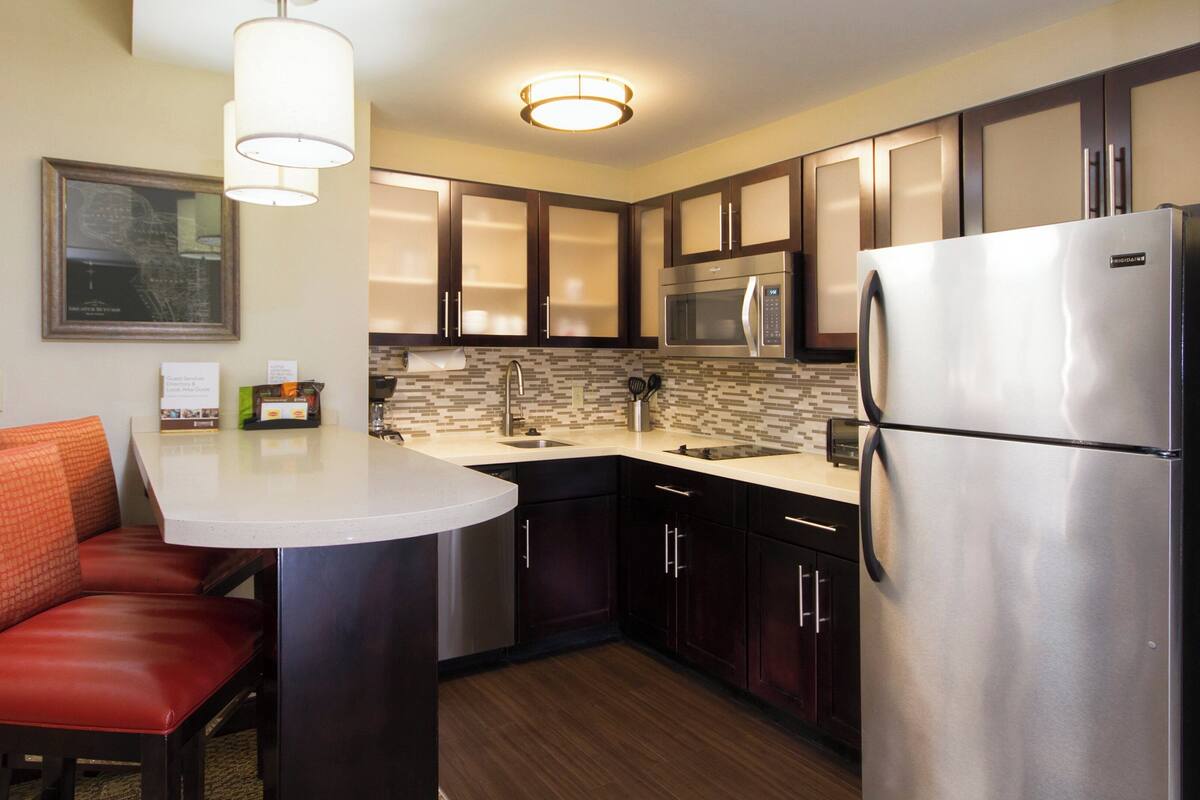 A compact kitchen with a refrigerator, microwave, and a small dining area with a chair.