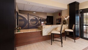 A reception area with a marble counter, two bar stools, a wall-mounted phone, and a decorative vase. - Staybridge Suites Buffalo-Amherst by IHG (Buffalo)