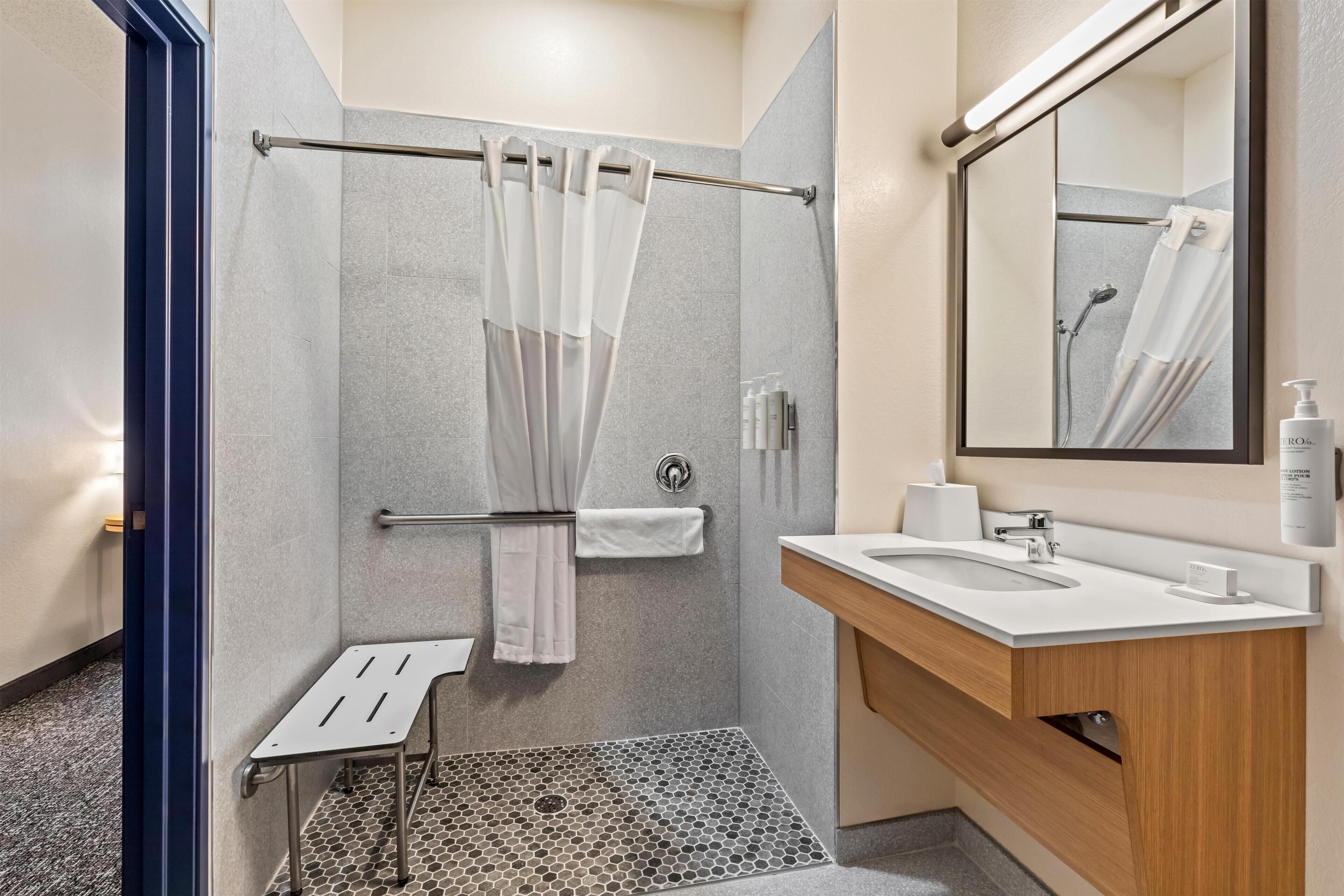 Een moderne badkamer met een douche, wastafel, spiegel en een klein opstapkrukje.