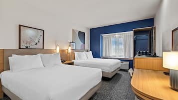 A hotel room with two beds, a desk, a chair, a window with curtains, and artwork on the walls.
