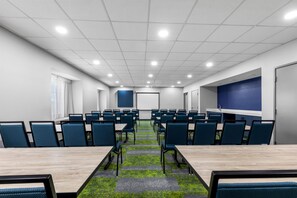 Un salón de conferencias con varias mesas y sillas, una pantalla de proyector y una pared azul de acento.