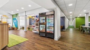 Un espacio interior moderno con suelo de madera, una zona de recepción, máquinas expendedoras y una pared verde.