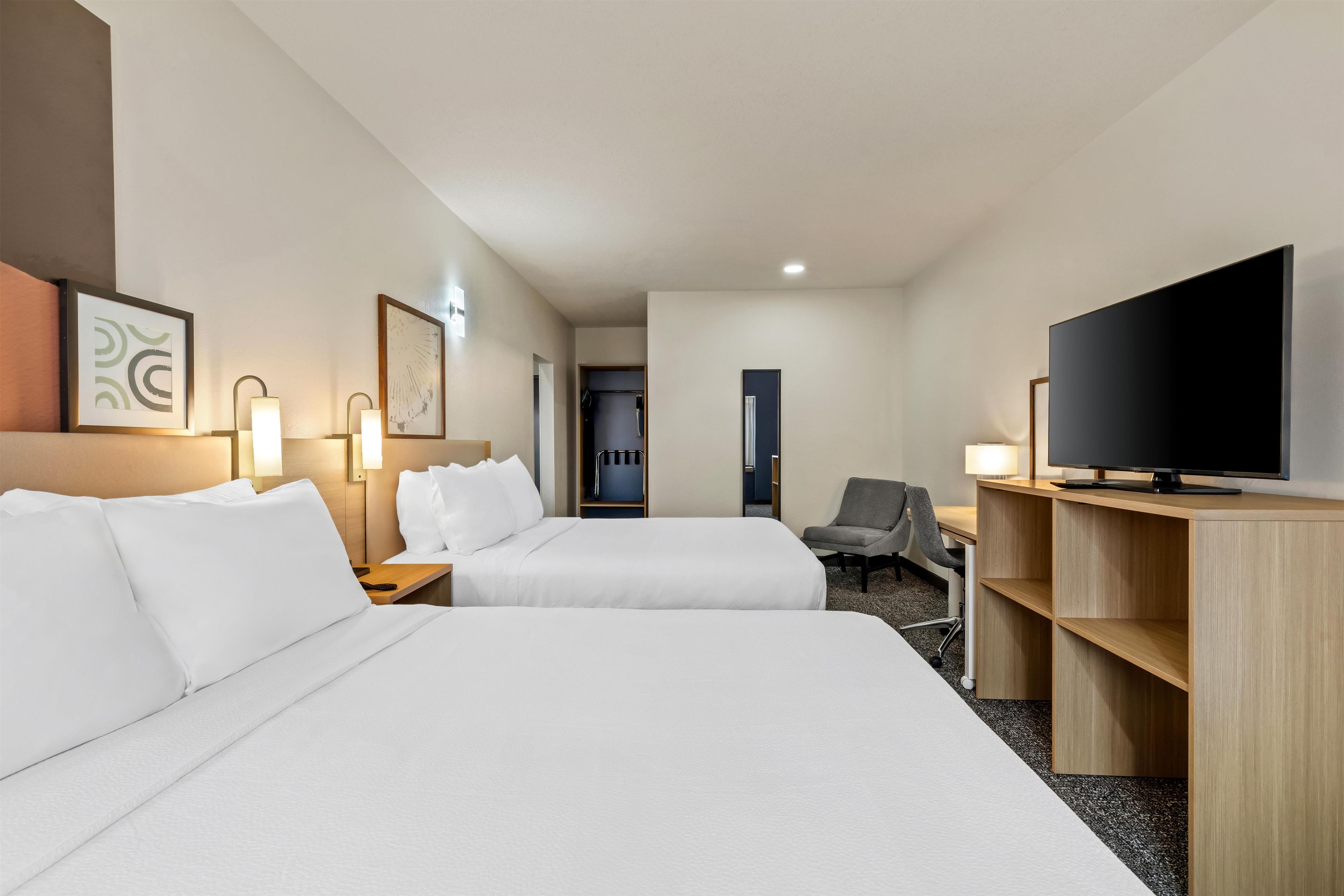 A hotel room with two beds, a desk with a television, and a chair.