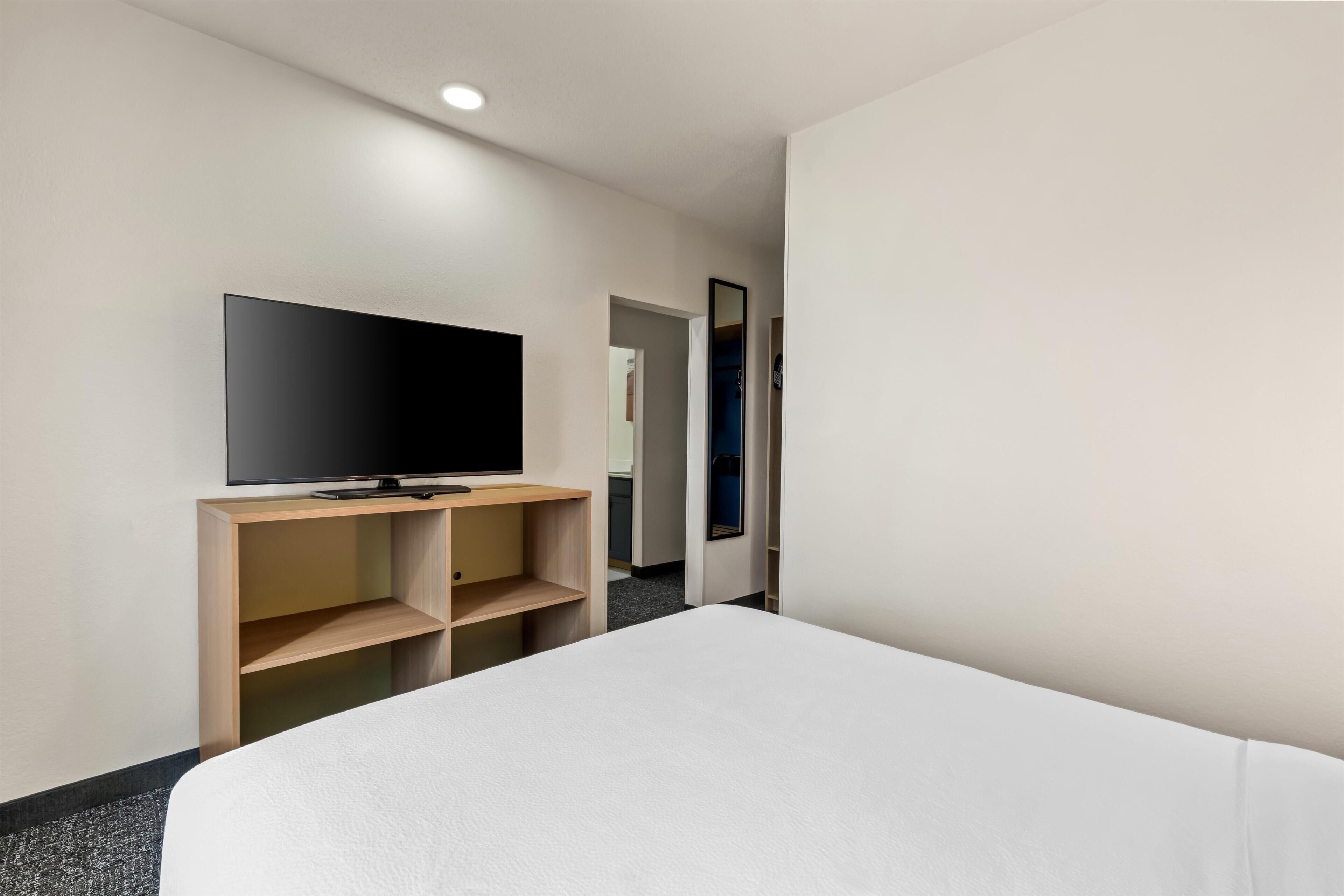 A hotel room with a bed, a TV on a wooden stand, and a mirror on the wall.