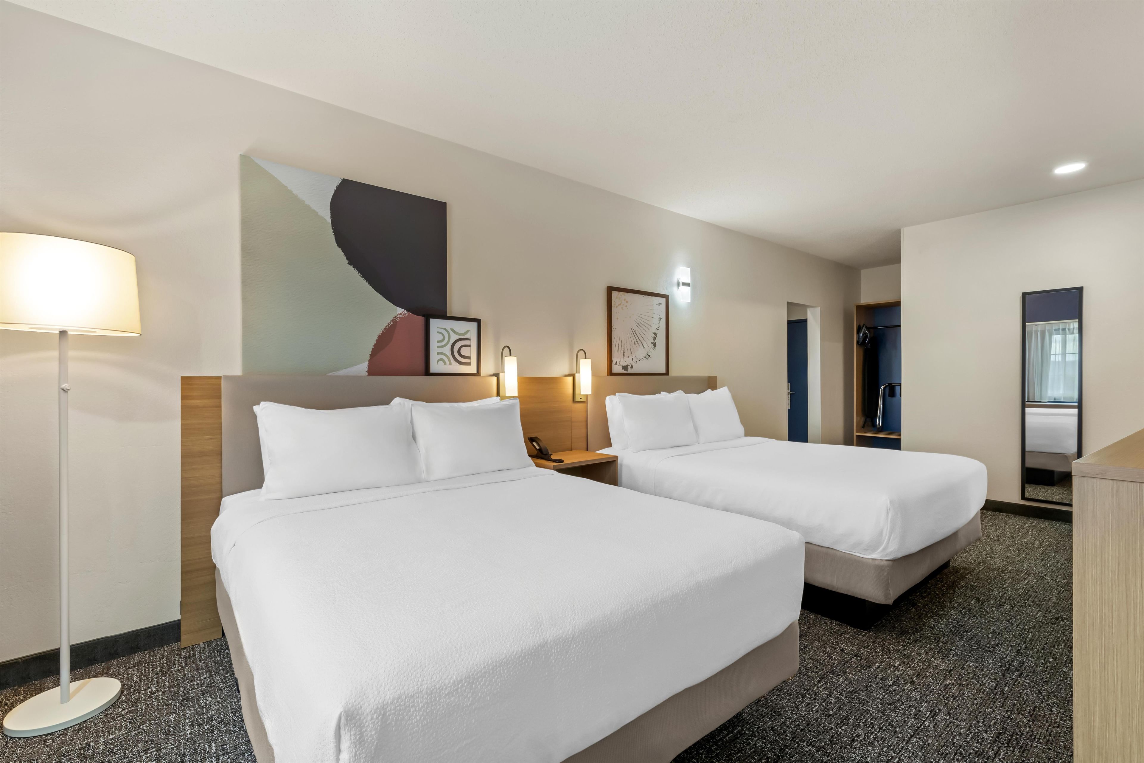 A hotel room with two beds, a desk, a lamp, and artwork on the wall.