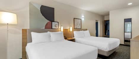 A hotel room with two beds, a desk, a lamp, and artwork on the wall.