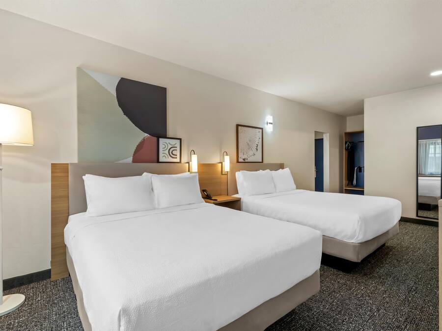 A hotel room with two beds, a desk, a lamp, and artwork on the wall.