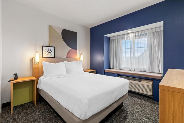 Una habitación de hotel con cama, mesitas de noche, una ventana con cortinas, una obra de arte en la pared y un radiador.