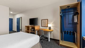 Habitación de hotel con cama, escritorio, silla, televisor, microondas y puerta con perchero.