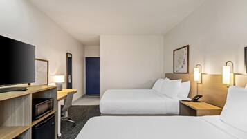 A hotel room with a television, desk, two beds, a door, and a wall-mounted artwork.