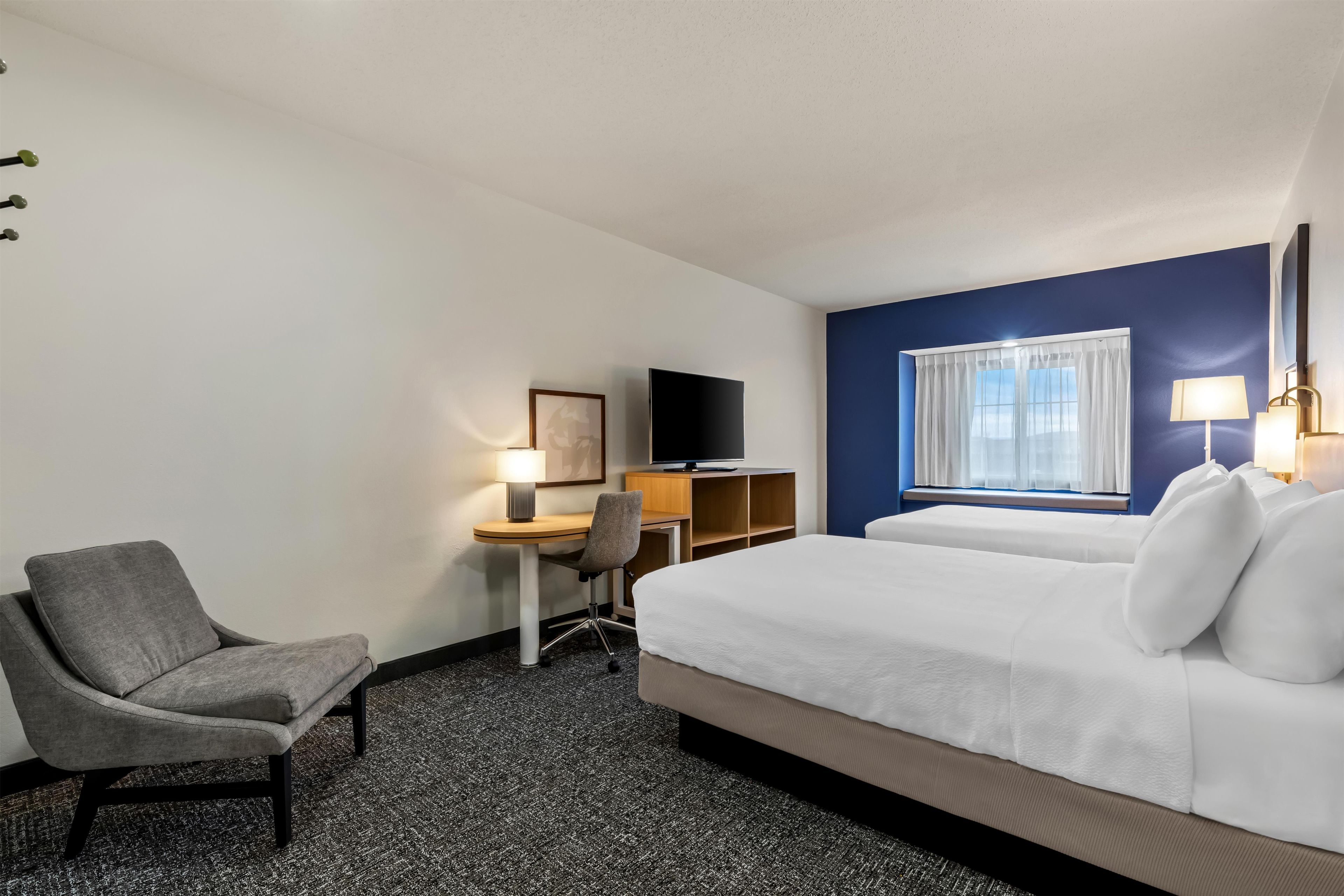 Une chambre d’hôtel équipée d’un lit, d’un bureau, d’une chaise, d’une télévision et d’une fenêtre avec des rideaux.