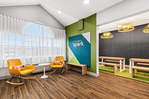 Un espacio de oficina moderno con un ventanal grande, una pared de acento verde y una zona de estar con un banco y sillas.