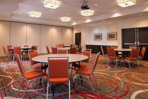 A conference room with round tables and orange chairs, equipped with a projector and ceiling lights. - Holiday Inn Express & Suites Monroe by IHG (Monroe)