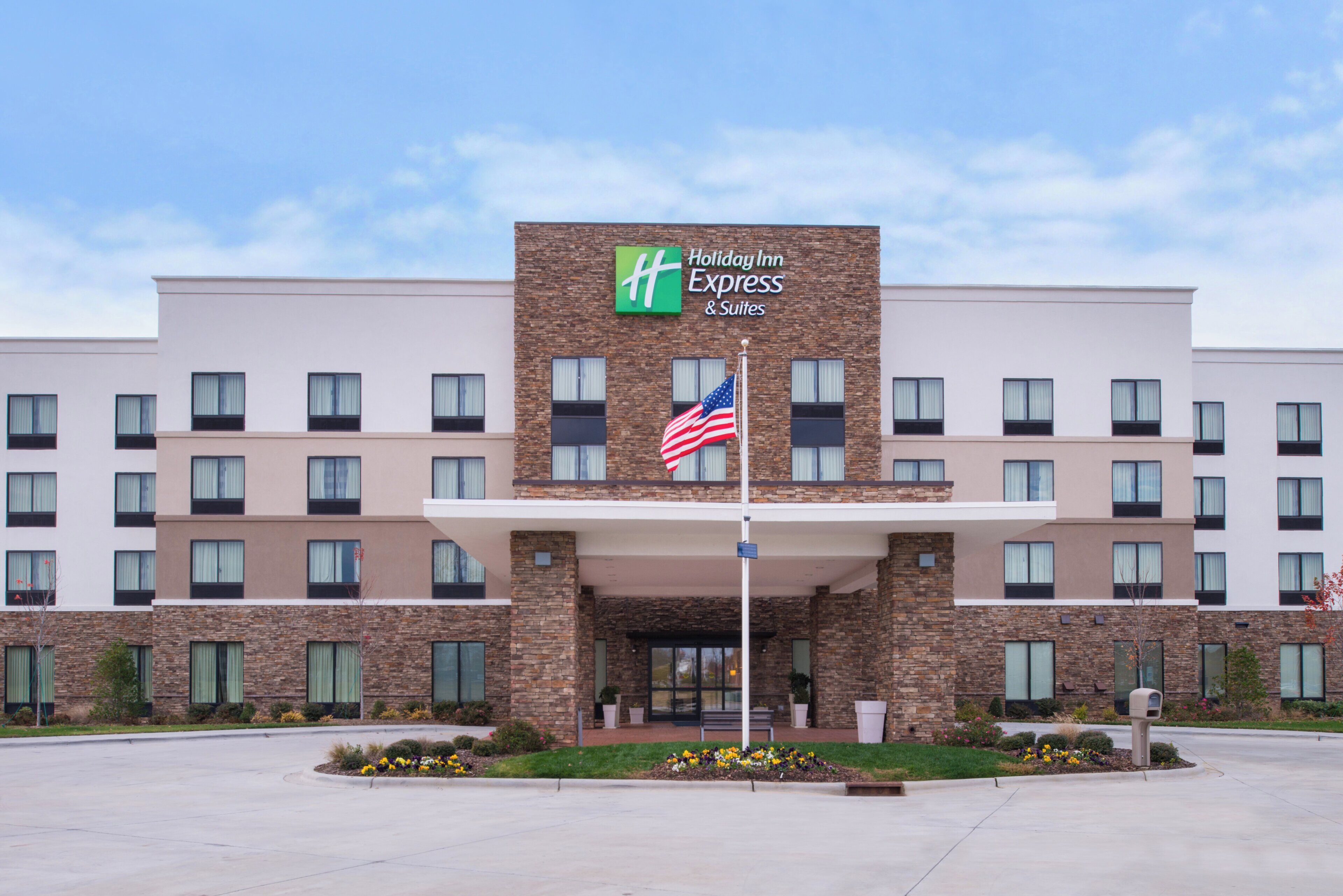 Un hôtel Holiday Inn Express & Suites doté d’une façade en pierre, de nombreuses fenêtres et arborant le drapeau américain.